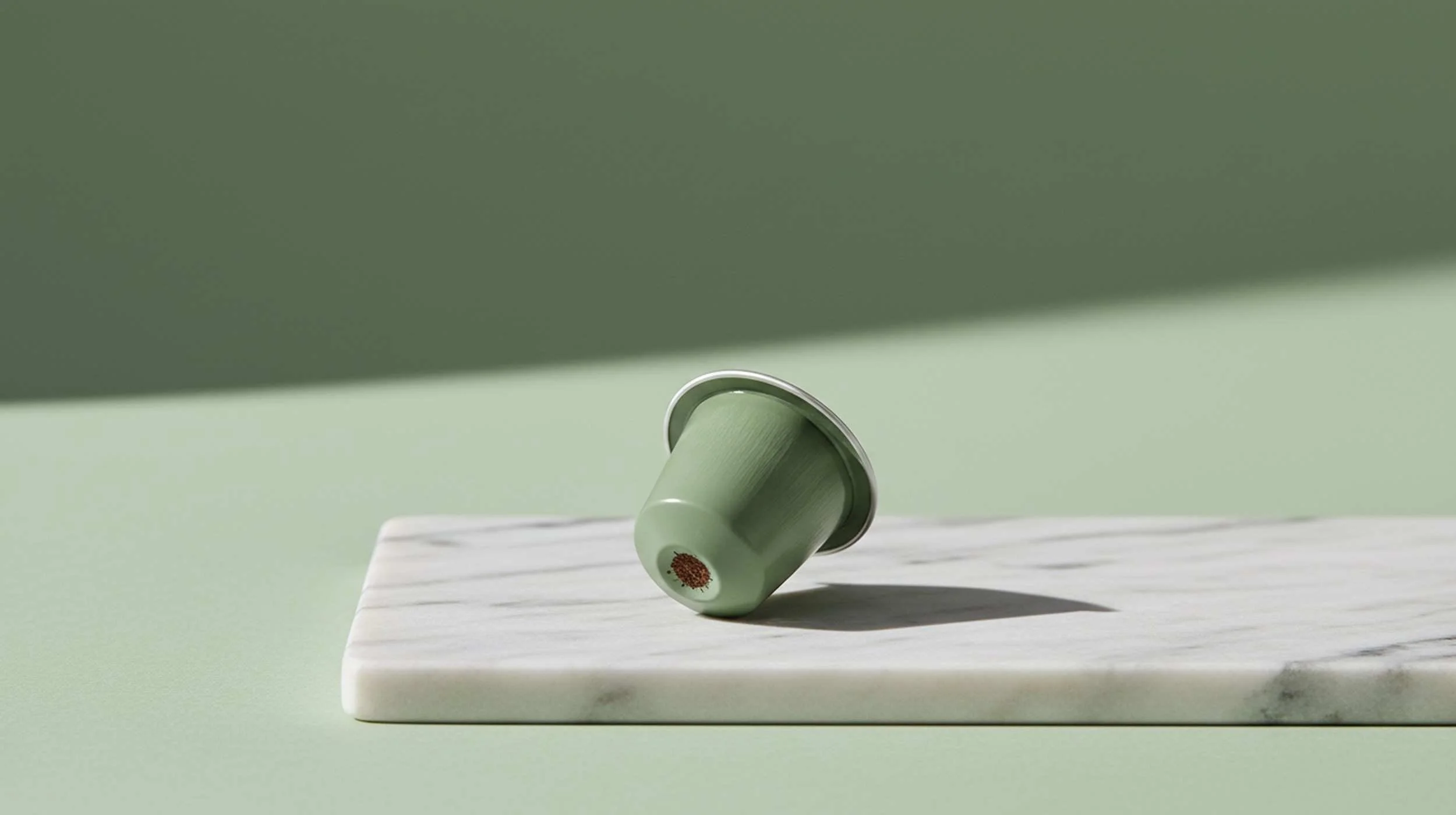 A flat-lay of seven decaf coffee pod boxes with Nespresso-compatible aluminium capsules, dark roasted coffee beans, ground coffee and a ceramic espresso cup on a white marble surface