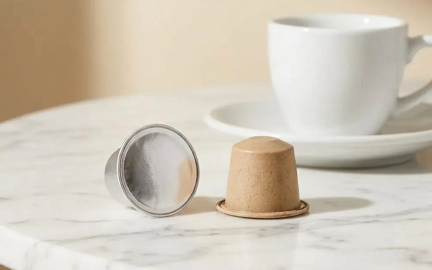Aluminium coffee capsule next to compostable bioplastic capsule on white marble, showing material contrast