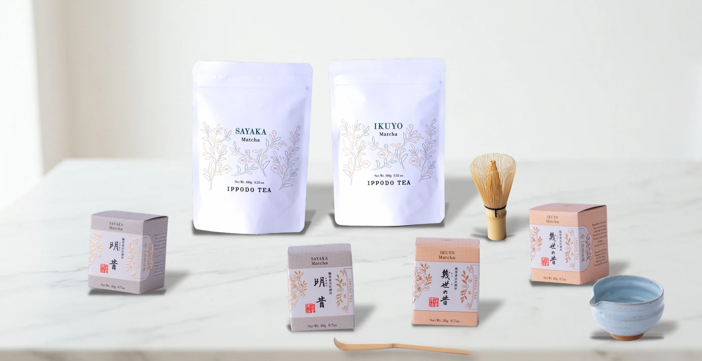 Ippodo Tea matcha in Sayaka and Ikuyo 100g pouches and 20g boxes, with a bamboo whisk, tea scoop and ceramic bowl on a white marble surface