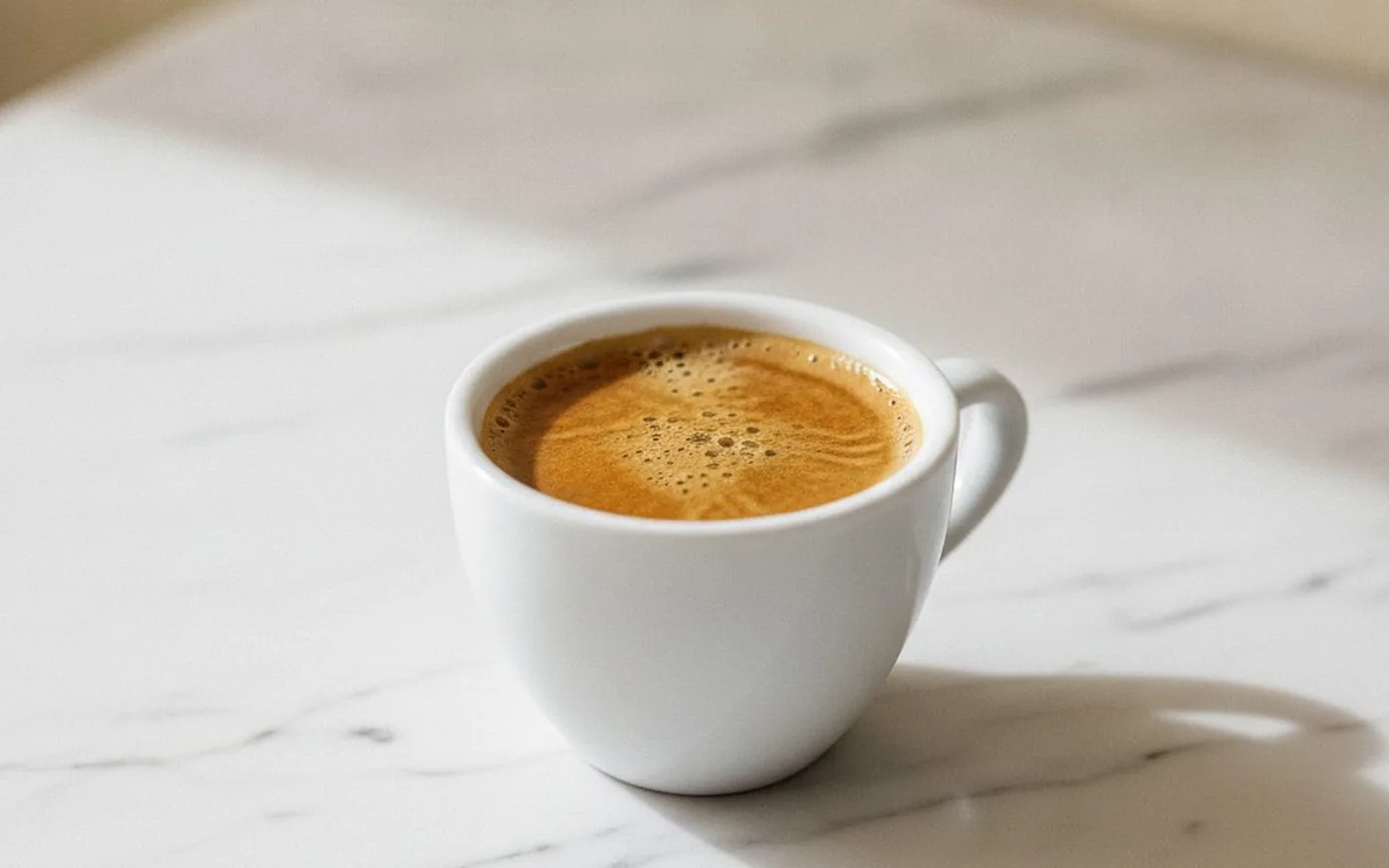 Espresso with golden crema in white ceramic cup on white marble surface