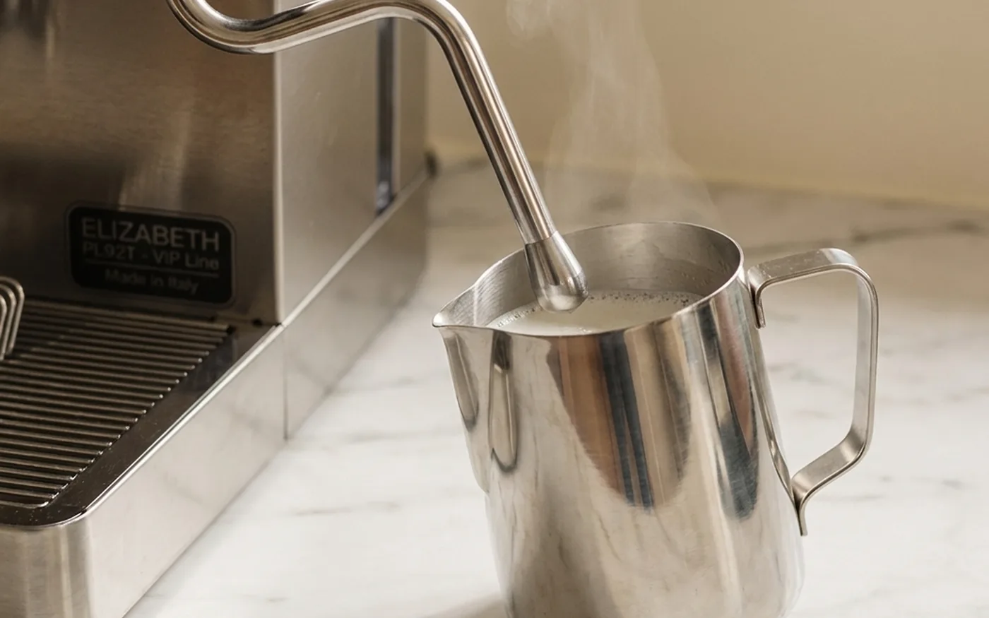Steam wand texturing milk in a stainless steel jug for a flat white