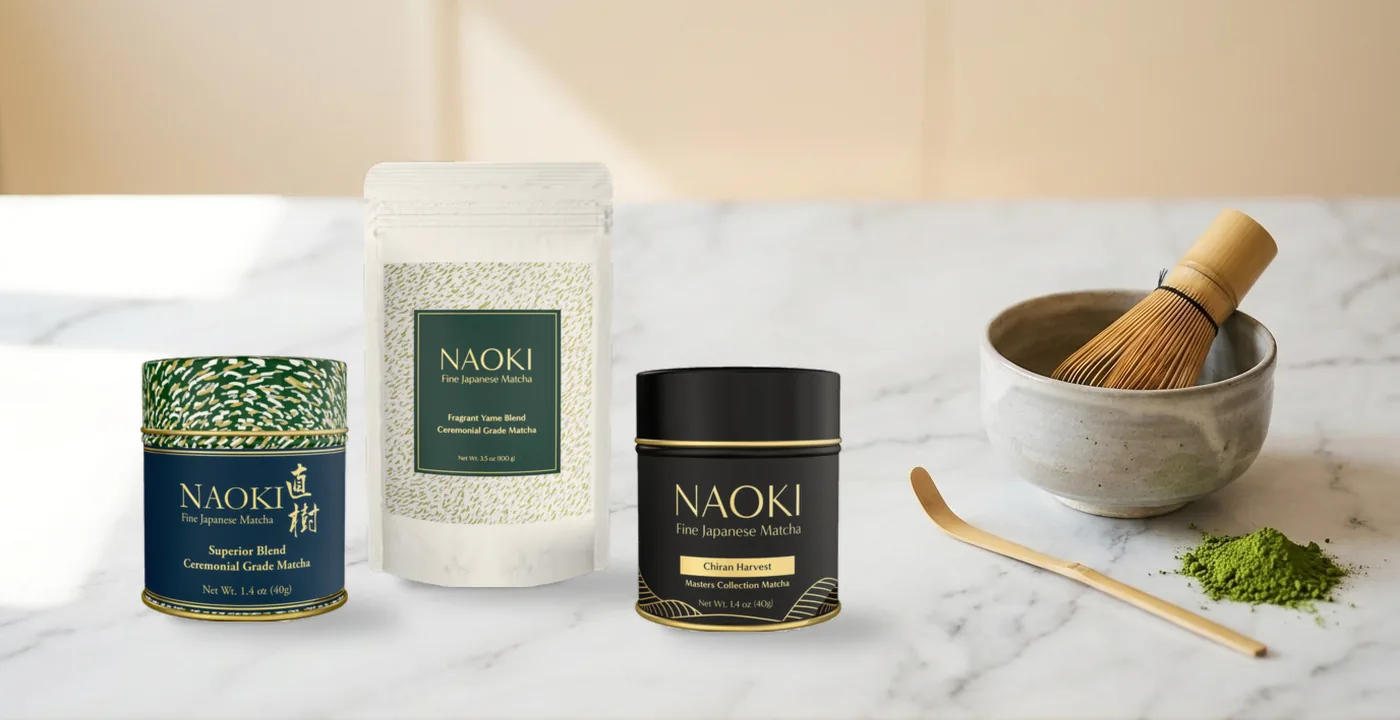 Three Naoki Matcha products - the Superior Blend tin, Fragrant Yame pouch and Chiran Harvest tin - beside a matcha bowl and bamboo whisk on white marble