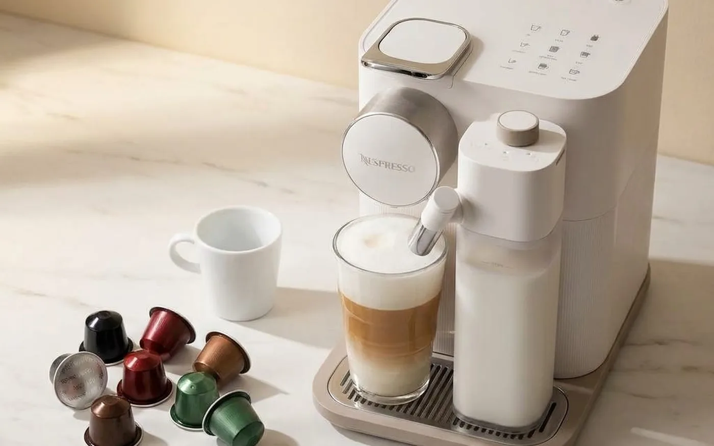 Assorted Nespresso Original Line capsules in various colours arranged on marble surface beside Gran Lattissima machine