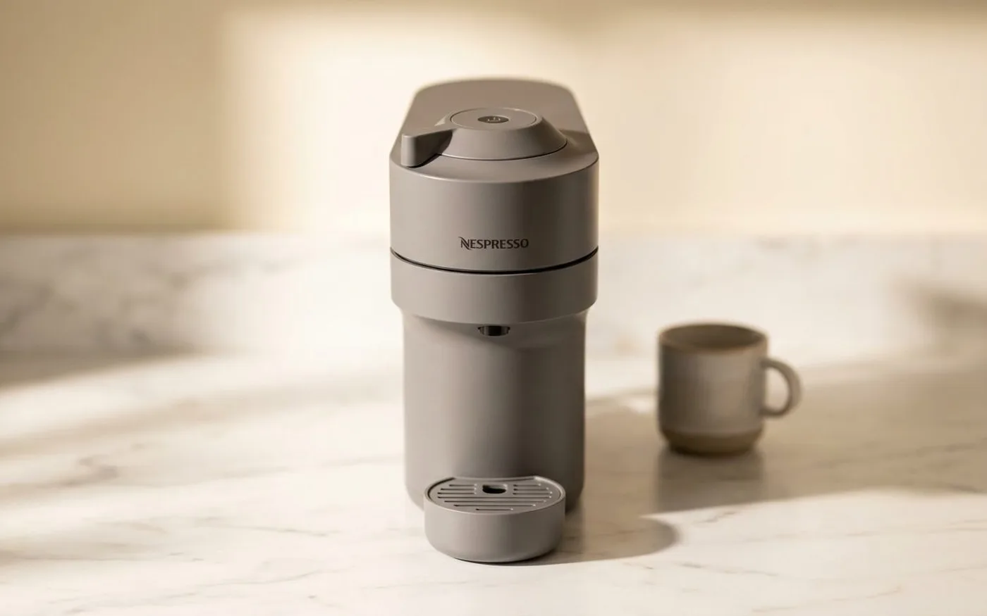 Nespresso Vertuo Pop compact coffee pod machine in grey on a white marble countertop