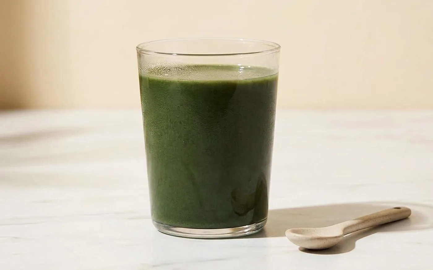 Rheal Clean Greens powder mixed into a glass of oat milk on a white marble countertop