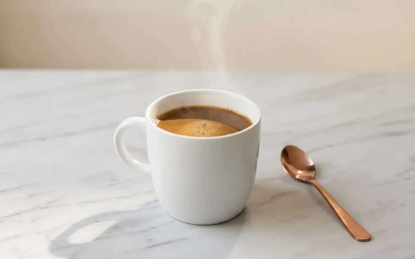 Single white ceramic mug of warm brown mushroom coffee with copper spoon on white marble in morning light